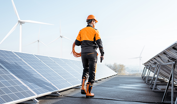 Man wearing an orange helmet working next to solar panels.