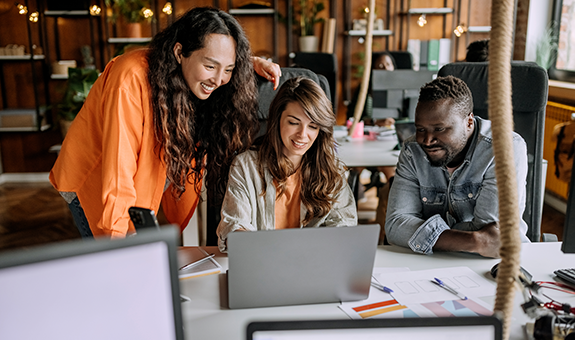 A Group Of People Smiling And Looking At A Laptop